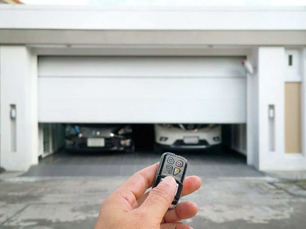 Hand holding garage door remote opening a garage.