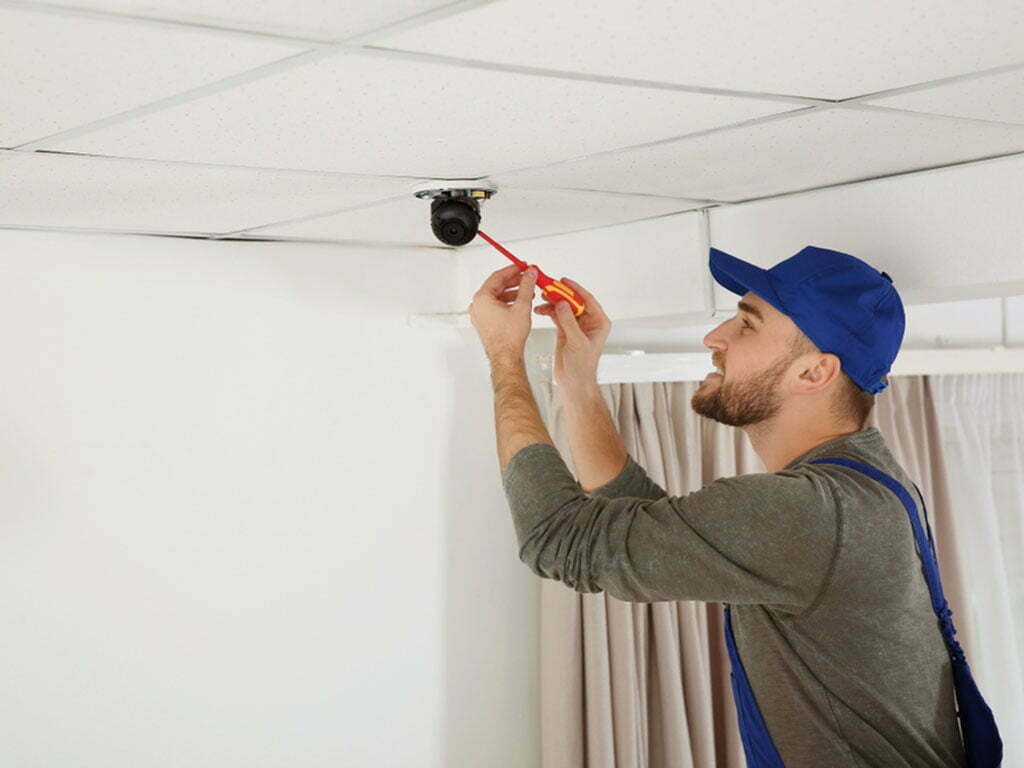 Man installing a security camera on a ceiling.
