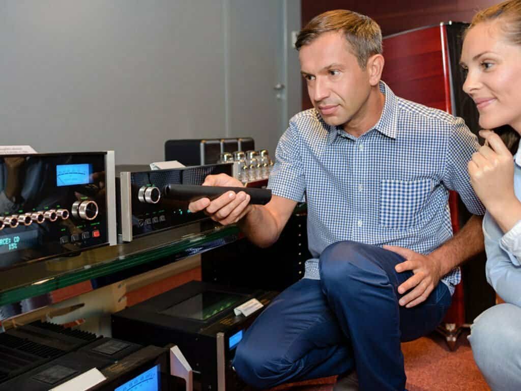 A man is demonstrating an audio system to a woman in a store.