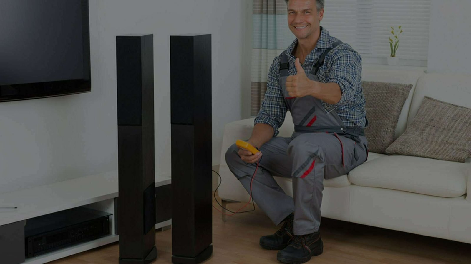 Man with tools gives thumbs up next to home theater speakers.