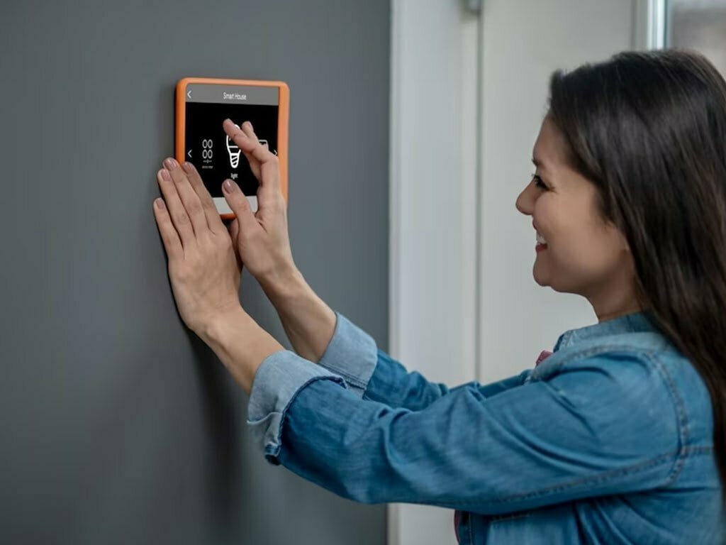 Smiling woman adjusting a smart home control panel.