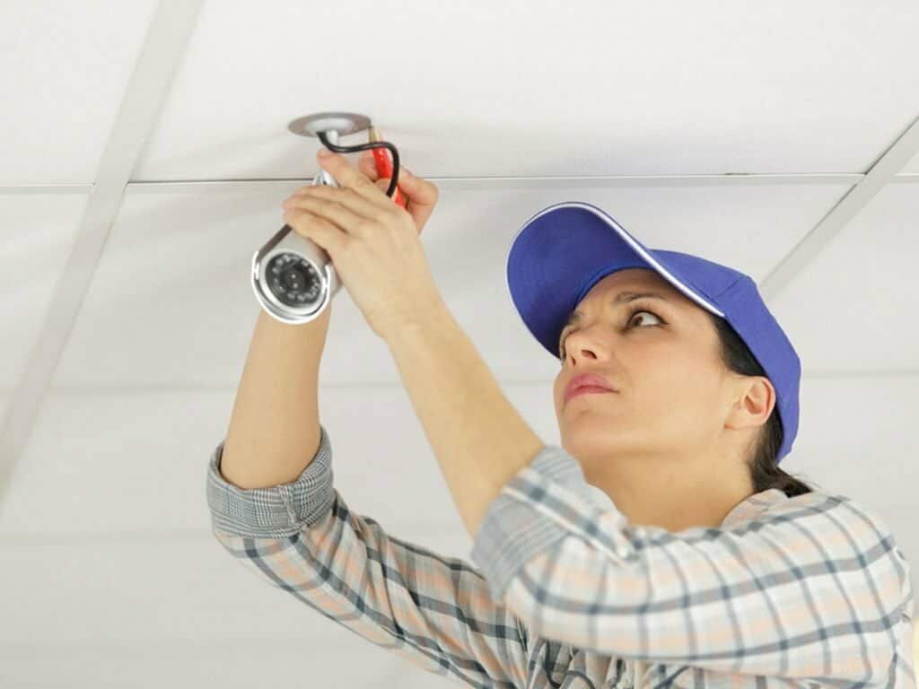 Woman installing a surveillance camera on a ceiling.