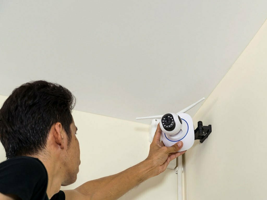 Man installing a white Wi-Fi security camera on a wall.