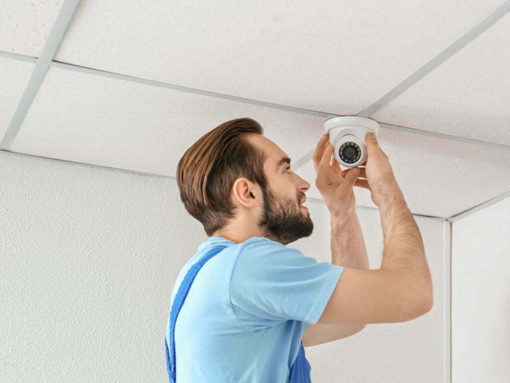 Man installing a white security camera on a ceiling.