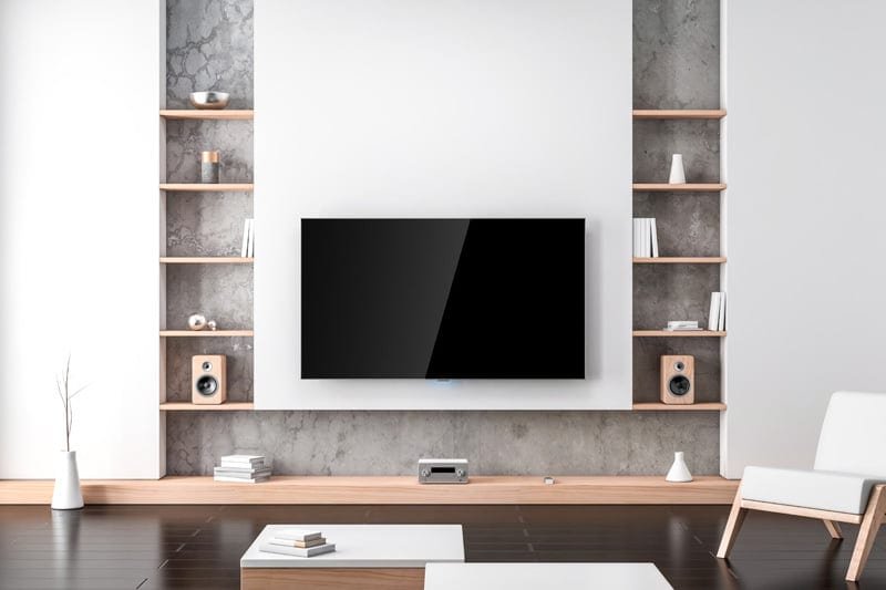 A large, modern flat-screen TV is mounted on a textured concrete wall, flanked by light wood shelves.