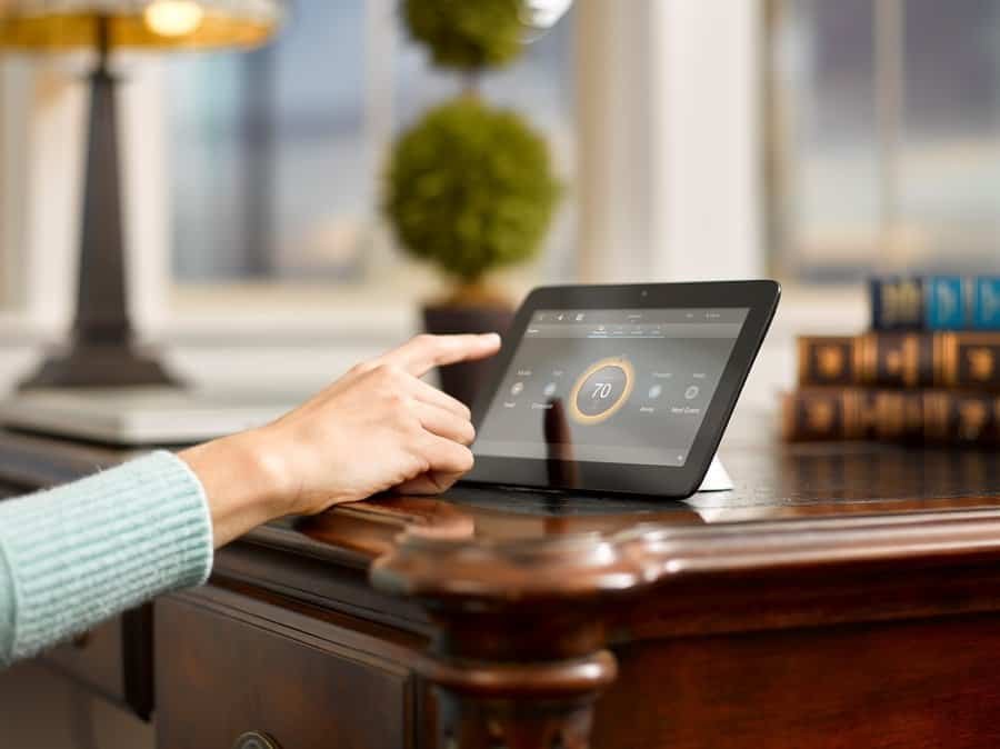 Hand adjusting smart home tablet on a wooden desk.