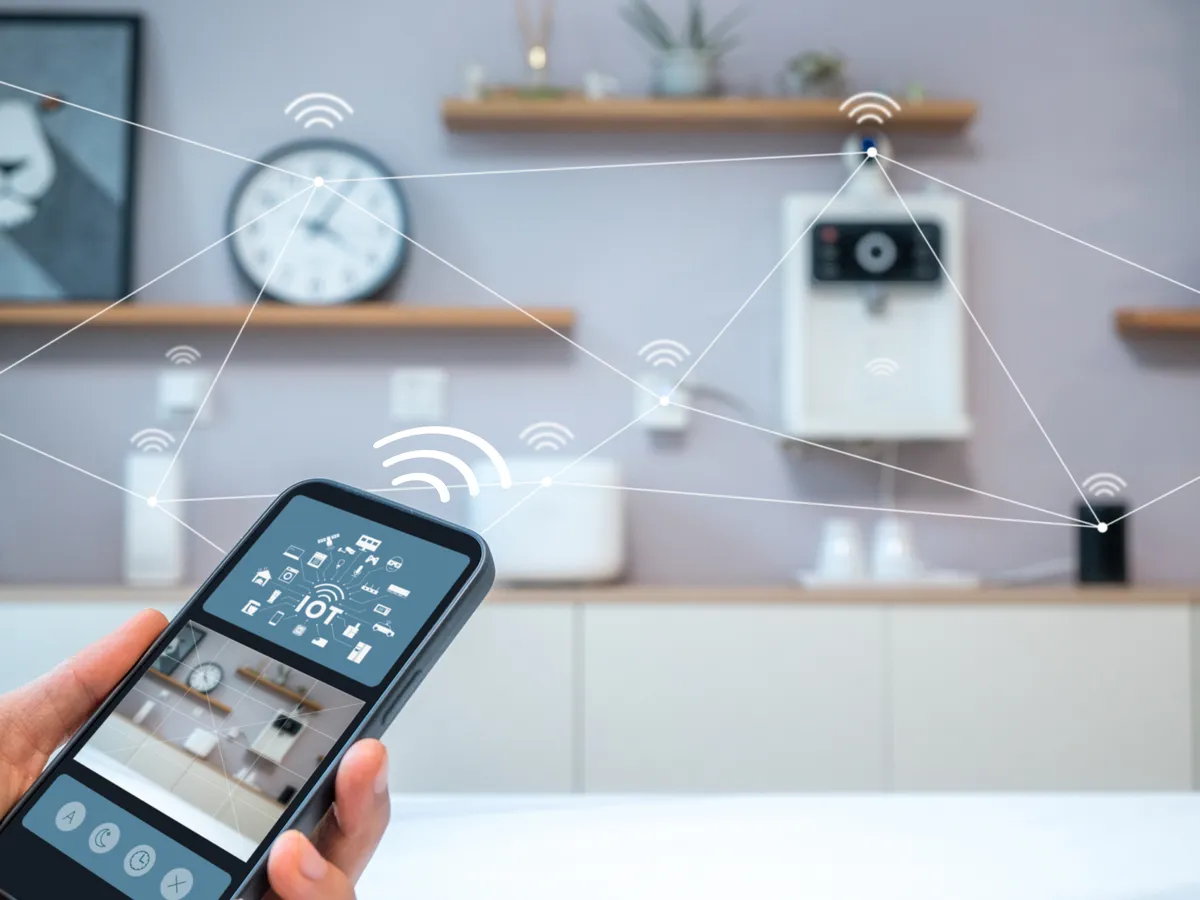 A hand holds a smartphone showing smart home controls, with signals linking devices