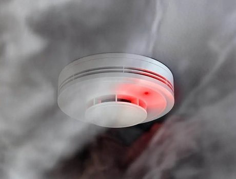 Smoke detector with a red light, surrounded by smoke.