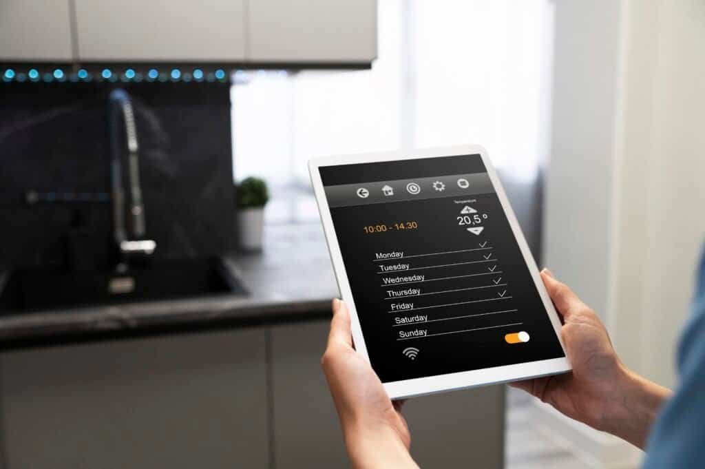 Hands holding a tablet displaying smart home controls in a kitchen.