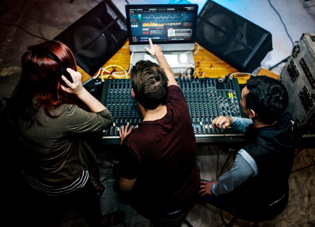 Three people working at an audio mixing console with a laptop.