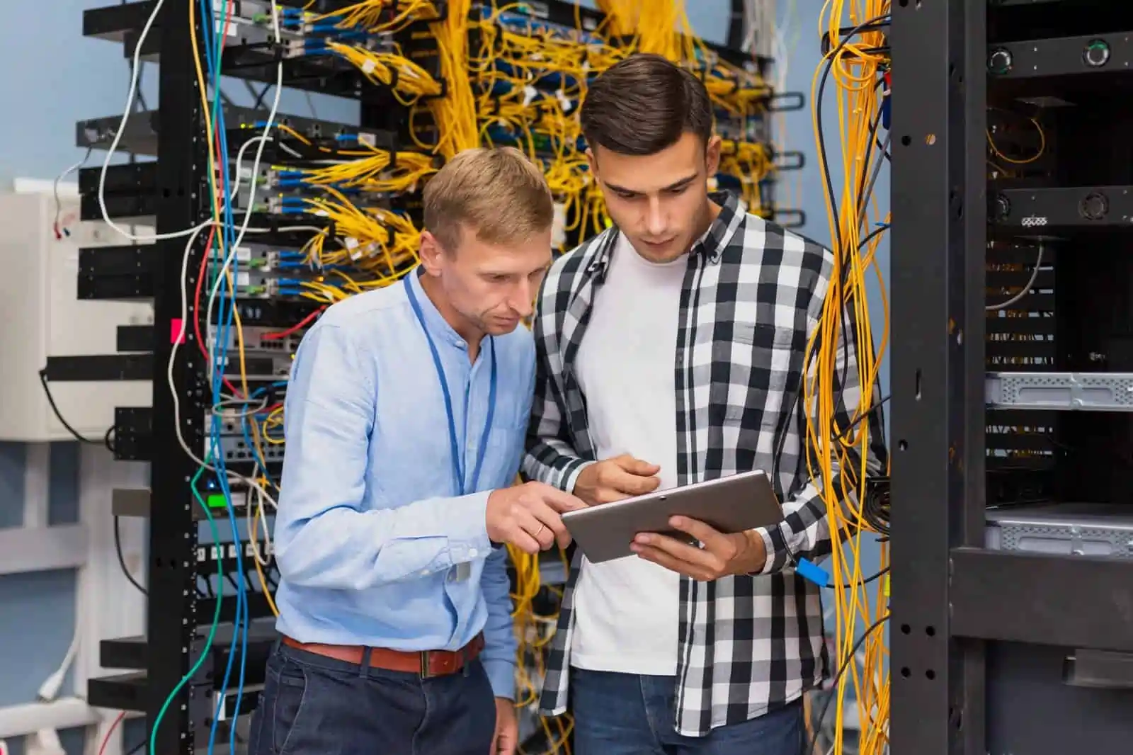 Two technicians examining a tablet in a server room.